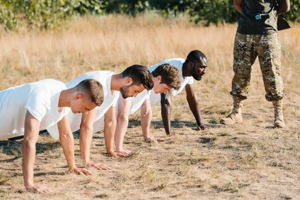 Candidats effectuant des pompes pour une épreuve de test physique de recrutement sous la surveillance d'un instructeur.