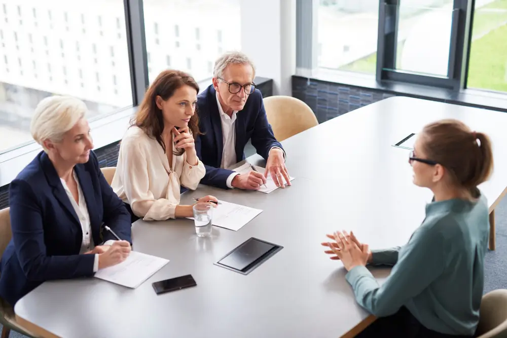 Jury de recrutement attentif écoutant une candidate et prenant des notes lors d'un entretien oral professionnel.