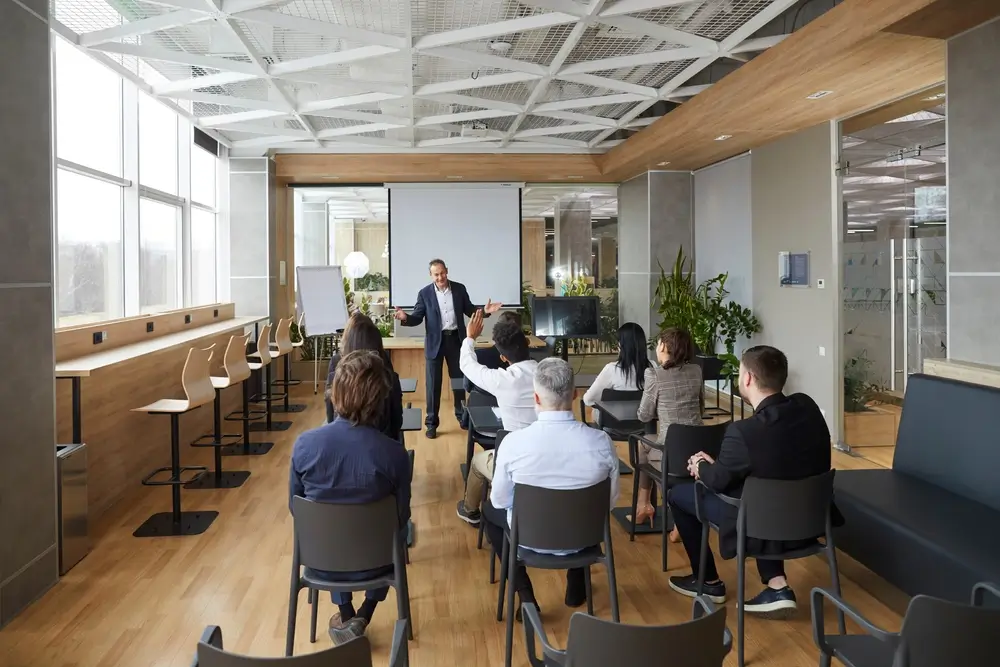 Jeunes adultes en formation professionnelle dans un centre, l'un lève la main face au formateur en salle de cours.