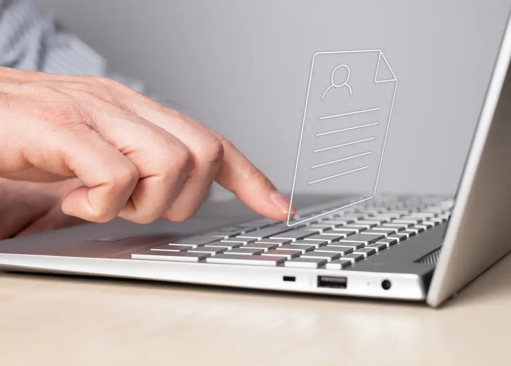 Main tapant sur un ordinateur portable avec une icône de CV pour soumettre une candidature en ligne.