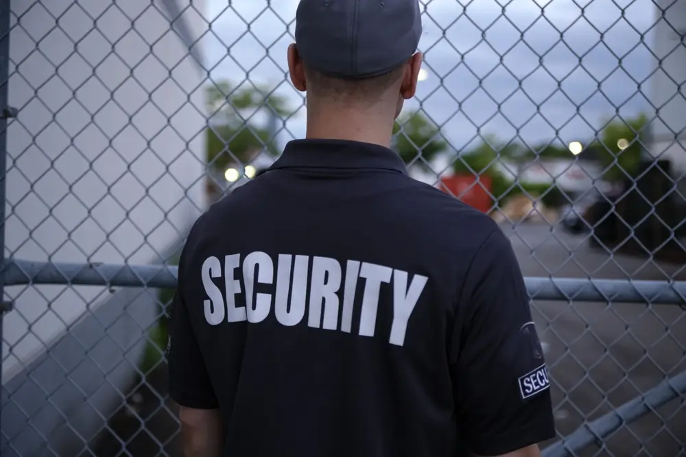 Agent de sécurité de dos en uniforme devant un grillage, illustrant le métier de surveillant pénitentiaire.