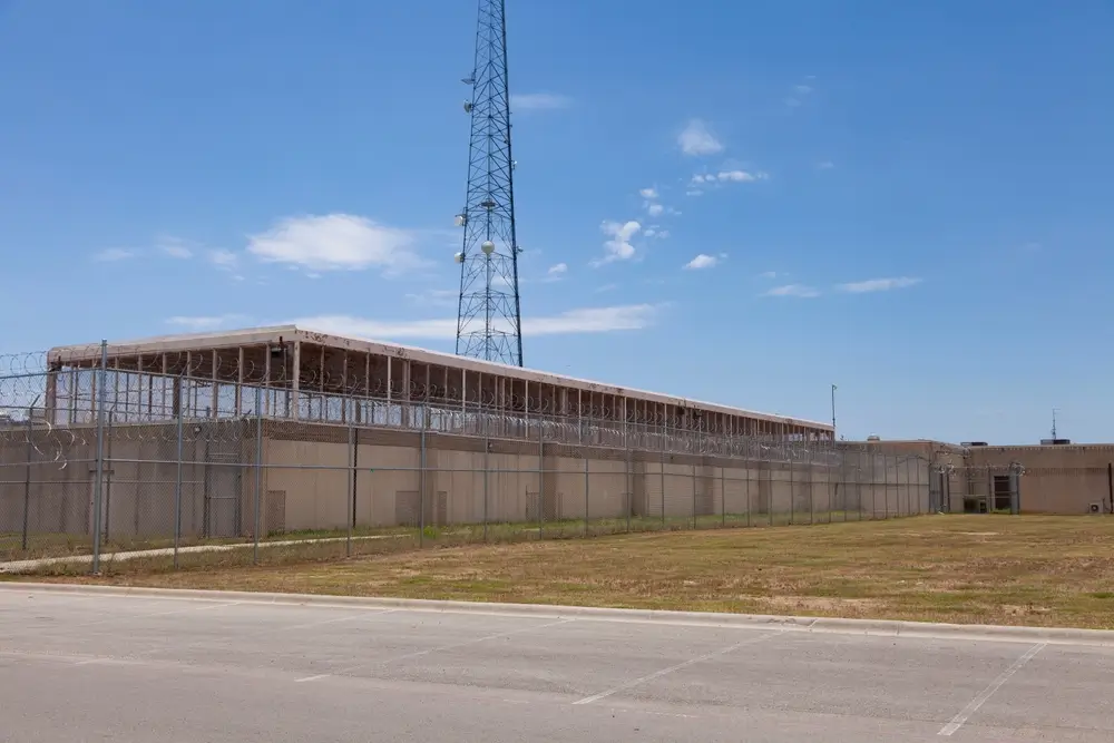 Façade d'un établissement pénitentiaire entourée de grillages et barbelés, vue extérieure d'une prison sécurisée.