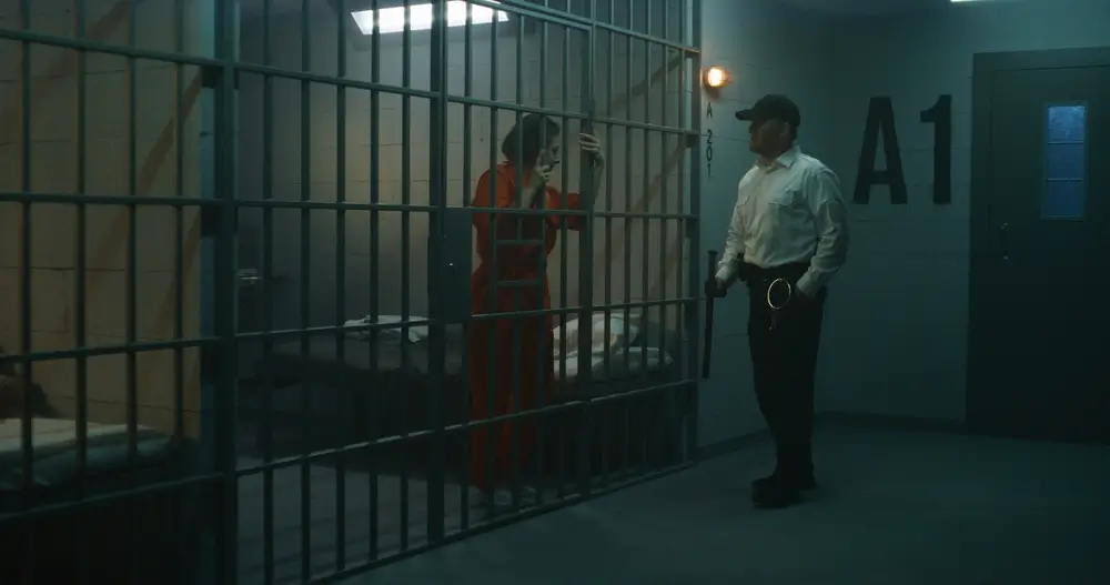 Agent pénitentiaire en uniforme blanc surveillant une détenue derrière les barreaux d'une cellule de prison.