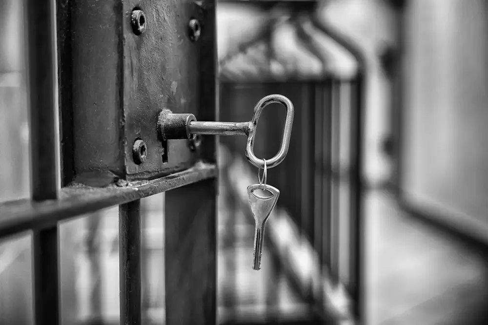 Clés de prison insérées dans le verrou d'une porte de cellule à barreaux dans un établissement pénitentiaire.