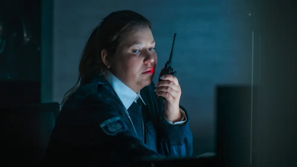 Agente pénitentiaire en uniforme utilisant une radio de surveillance pour assurer la sécurité en milieu carcéral.