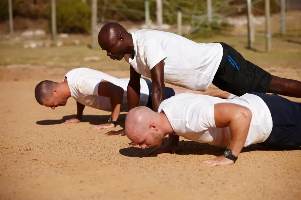 Trois recrues effectuent des pompes lors d'un exercice d'entraînement physique en groupe durant leur formation.