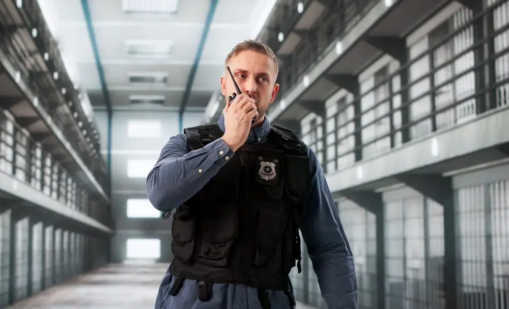Agent pénitentiaire en uniforme utilisant son talkie-walkie dans un couloir de centre pénitentiaire.