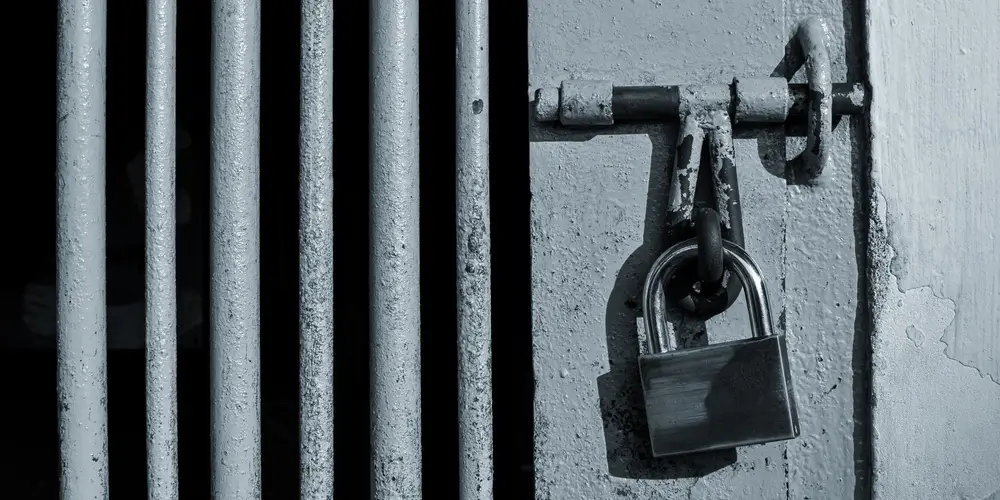 Cadenas de sécurité et verrou sur une porte de prison aux barreaux métalliques.