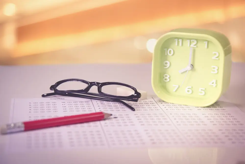 Minuteur vert, lunettes et crayon sur une feuille de test, illustrant la gestion du temps lors d'un examen.