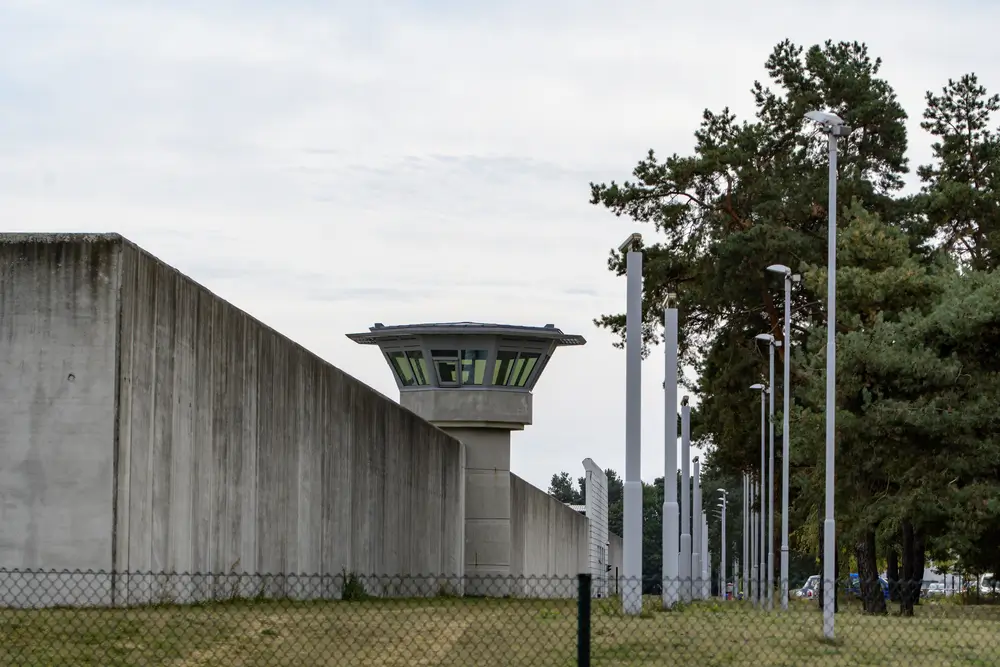 Haut mur d'enceinte et mirador de surveillance d'une prison, illustrant la présence constante des agents de sécurité.
