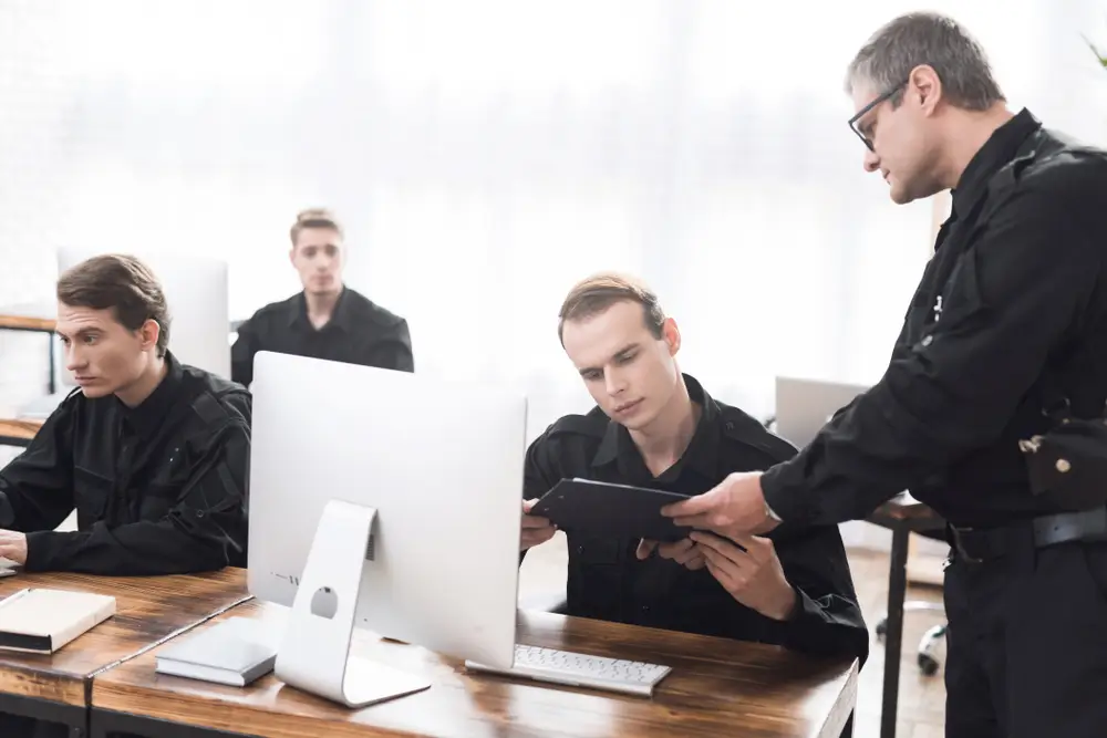Mentor guidant une recrue lors d'une session de formation d'agent pénitentiaire devant un poste informatique.